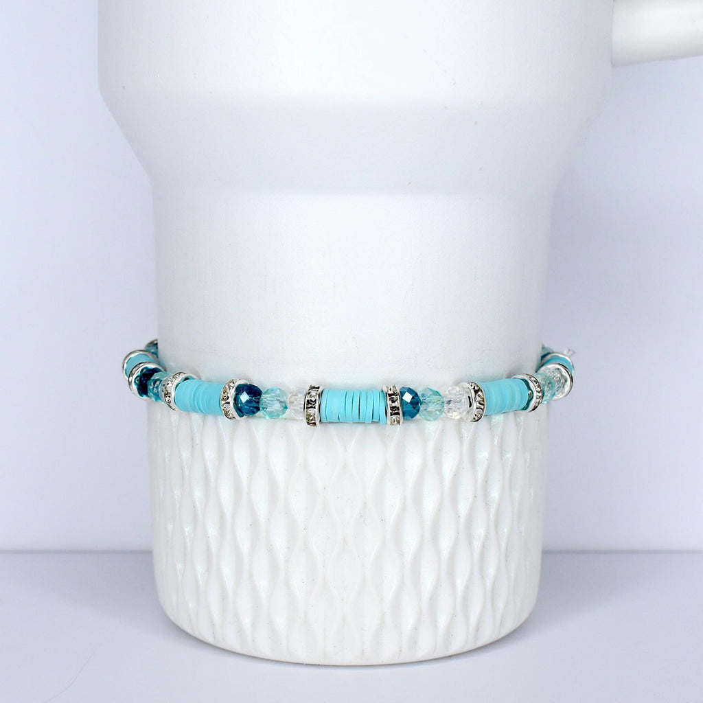 A turquoise beaded bracelet with silver accents and clear and blue crystal beads. The bracelet is displayed on a white, textured ceramic surface. The bracelet features a mix of round and flat beads.
