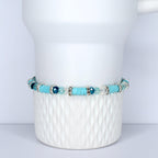 A turquoise beaded bracelet with silver accents and clear and blue crystal beads. The bracelet is displayed on a white, textured ceramic surface. The bracelet features a mix of round and flat beads.