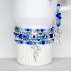 A collection of blue beaded bracelets with silver accents and charms. The bracelets feature various shades of blue beads, including light blue, dark blue, and clear beads. Silver bow-shaped charms dangle from the bracelets. The bracelets are displayed on a white Stanley.