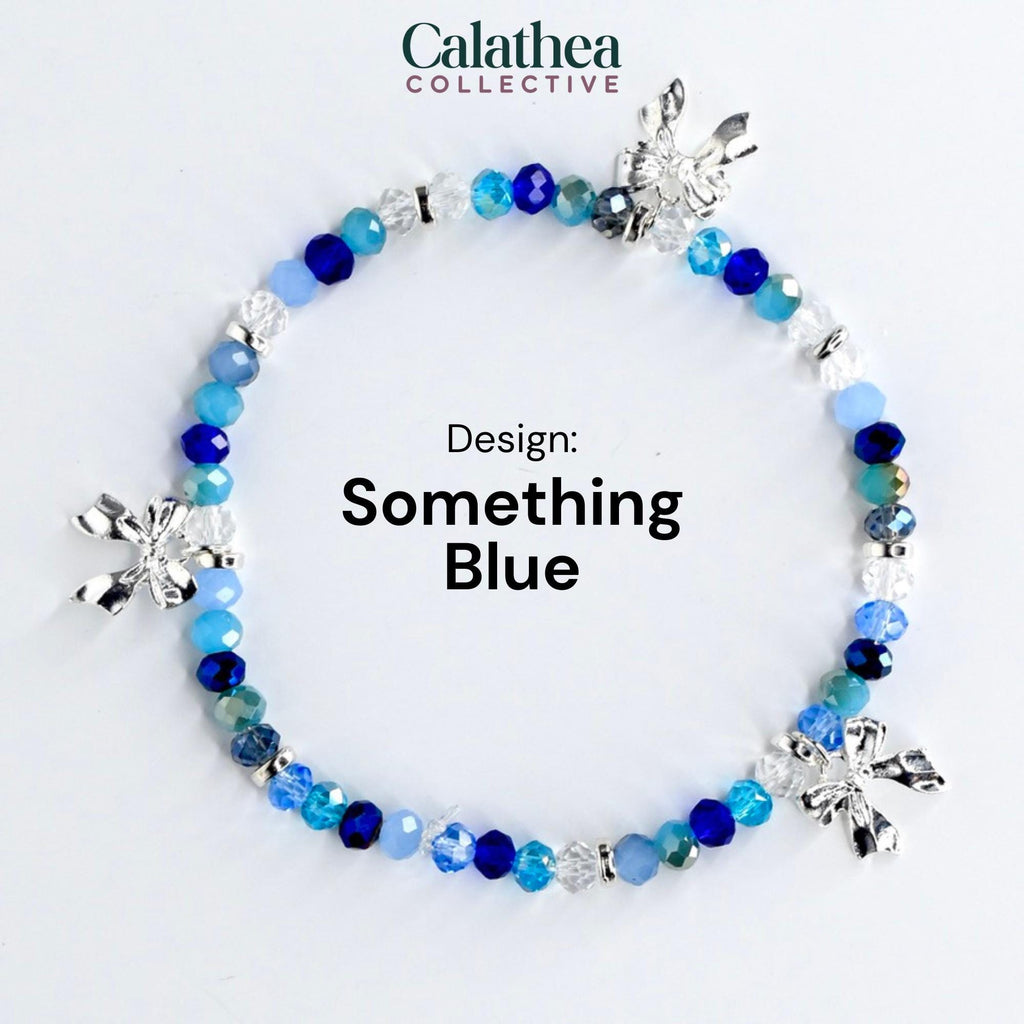 A beaded bracelet with a variety of blue beads and silver bow charms. The bracelet is labeled "Something Blue" and is from the Calathea Collective.