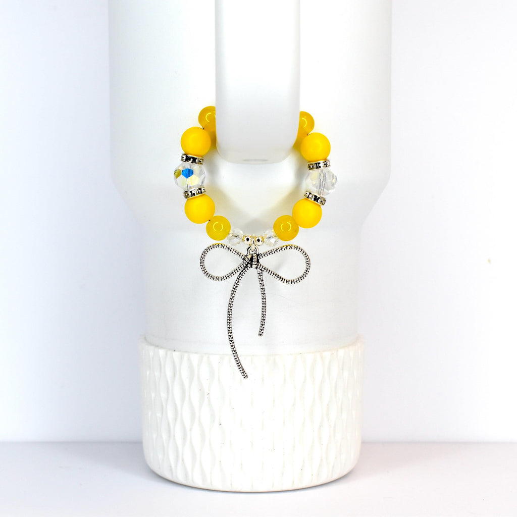 A yellow beaded bracelet with a silver bow charm. The bracelet features large, round yellow beads interspersed with clear, sparkling beads. The bow charm hangs below the bracelet, adding a touch of elegance.