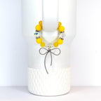 A yellow beaded bracelet with a silver bow charm. The bracelet features large, round yellow beads interspersed with clear, sparkling beads. The bow charm hangs below the bracelet, adding a touch of elegance.
