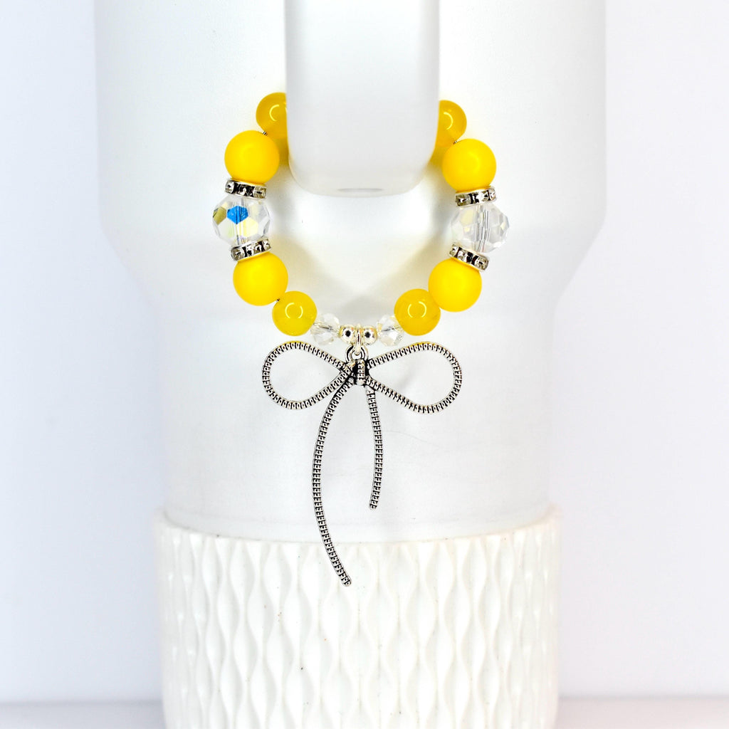 A yellow beaded tumbler handle bracelet with a silver bow charm. The bracelet features large, round yellow beads interspersed with clear, faceted beads. The silver bow charm hangs from the center of the bracelet, adding a touch of elegance.