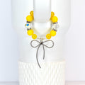 A yellow beaded tumbler handle bracelet with a silver bow charm. The bracelet features large, round yellow beads interspersed with clear, faceted beads. The silver bow charm hangs from the center of the bracelet, adding a touch of elegance.