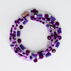 A collection of purple and clear beaded bracelets. The bracelets feature a variety of bead shapes and sizes, including round, cylindrical, and faceted beads. The color palette includes shades of purple and clear, with some iridescent accents.