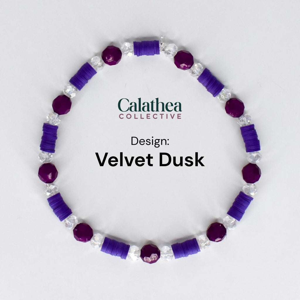 A bracelet with the text "Calathea Collective" and "Design: Velvet Dusk". The bracelet features alternating purple and clear beads. The purple beads are round and cylindrical, while the clear beads are faceted.
