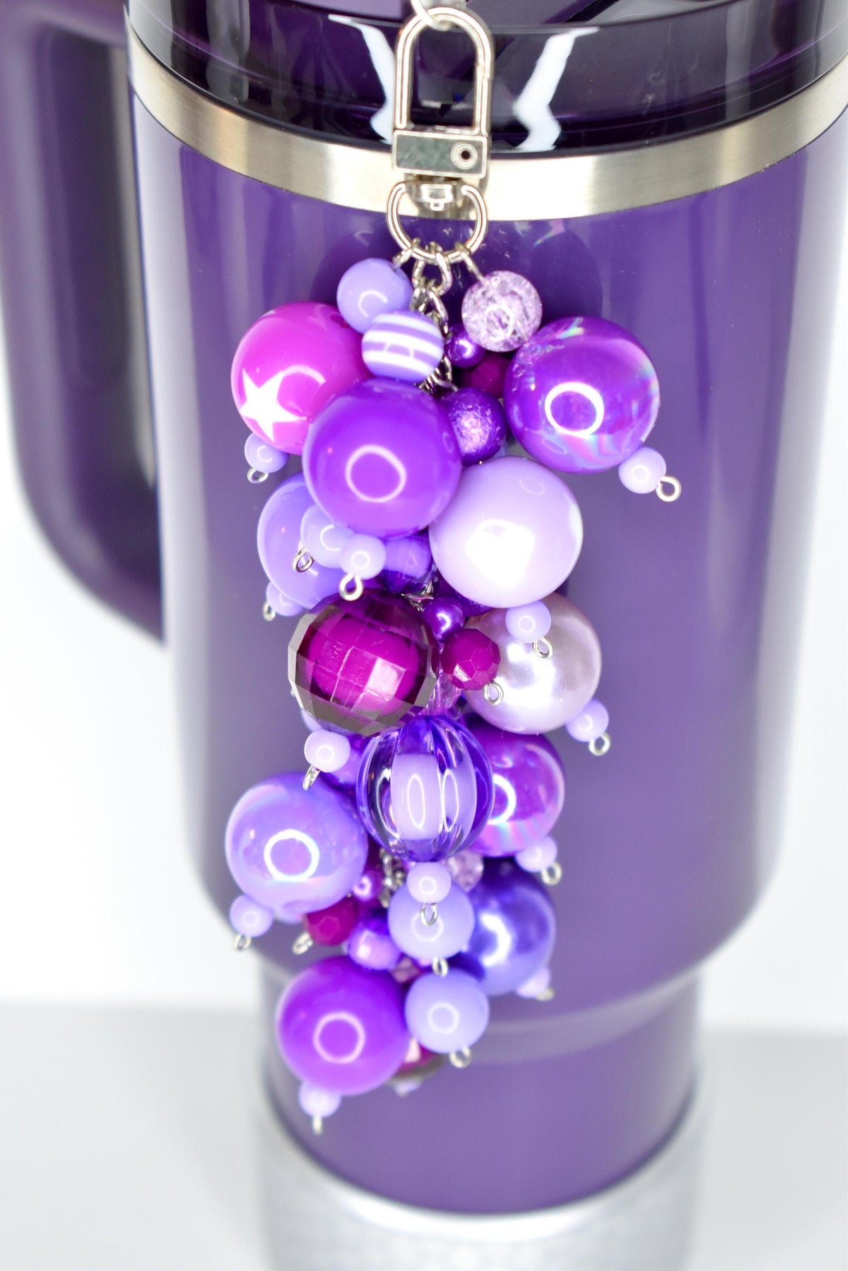 A purple tumbler with a beaded charm. The charm features a cluster of various sized purple beads, including round, faceted, and striped designs. The beads range in shades from light lavender to deep violet.