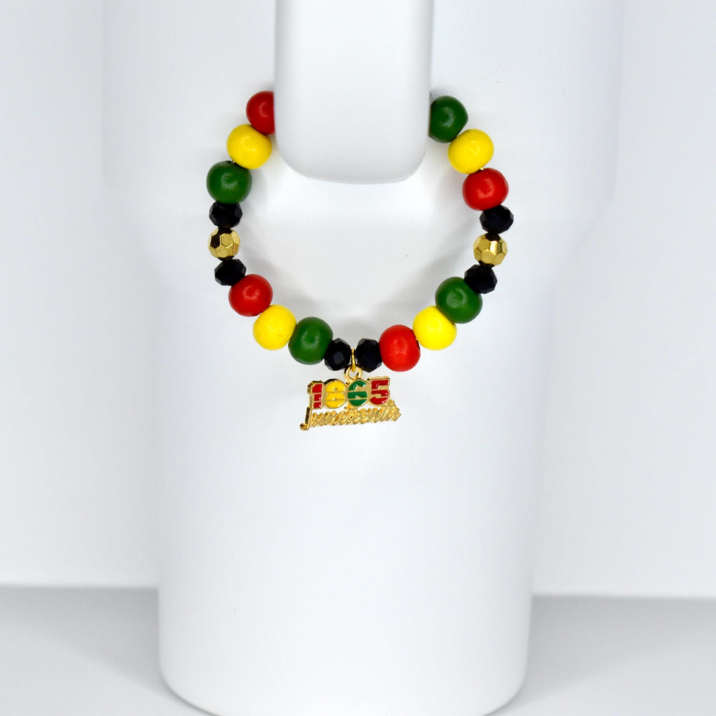 A beaded tumbler handle charm with red, yellow, green, black, and gold beads. A gold charm with the text "1865 Juneteenth" hangs from the bracelet. The bracelet is displayed on a white form.