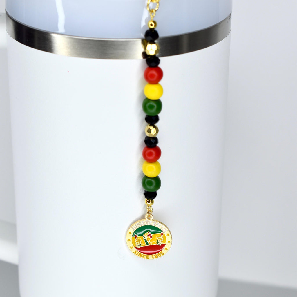 A white Stanley with a straw charm with Juneteenth themed charms. Features red, yellow, green, black, and gold beads.