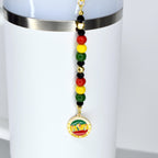 A white Stanley with a straw charm with Juneteenth themed charms. Features red, yellow, green, black, and gold beads.