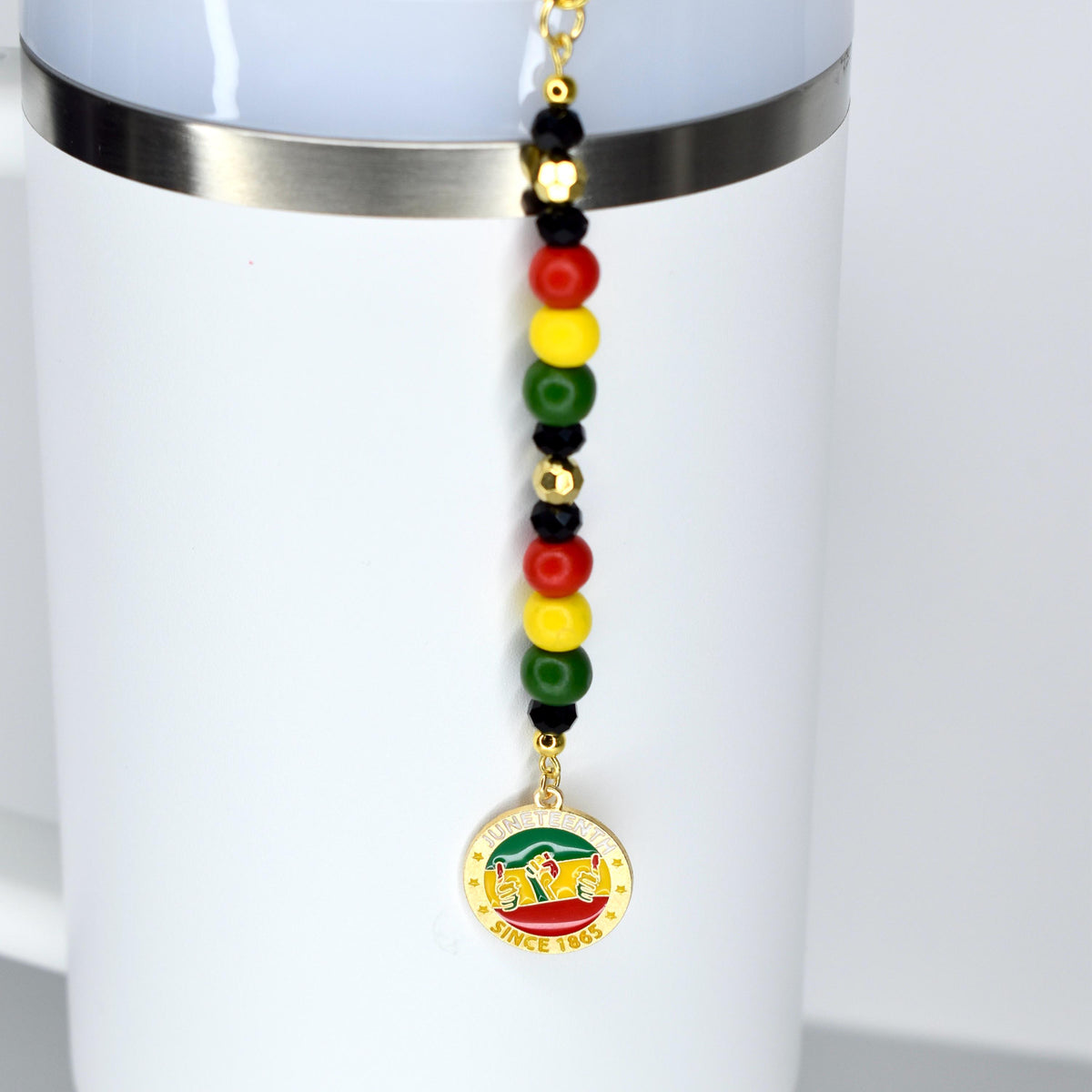 A white Stanley with a straw charm with Juneteenth themed charms. Features red, yellow, green, black, and gold beads.