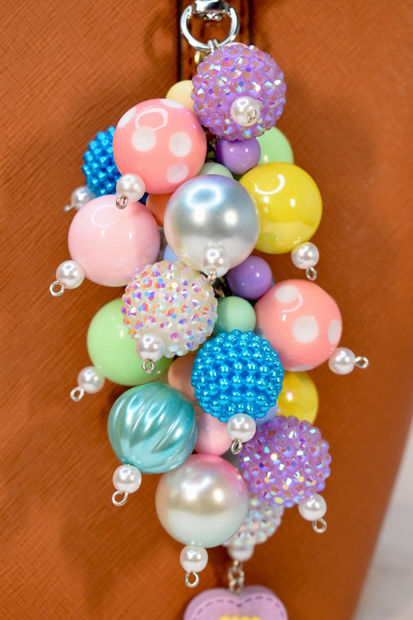 A colorful beaded charm featuring a variety of round beads in pastel shades of pink, blue, green, and yellow. Some beads have a textured, crystal-like surface, while others are smooth or dotted. Each bead is accented with a small pearl.