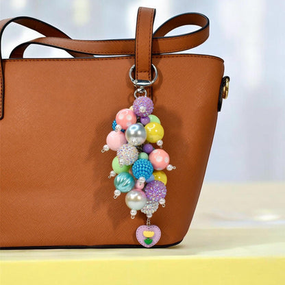 Pastel spring bag charm with colorful beaded cluster featuring glossy and textured beads in pink, yellow, blue, purple, and green, finished with pearl accents and a heart flower charm. Whimsical handmade purse accessory and statement keychain.