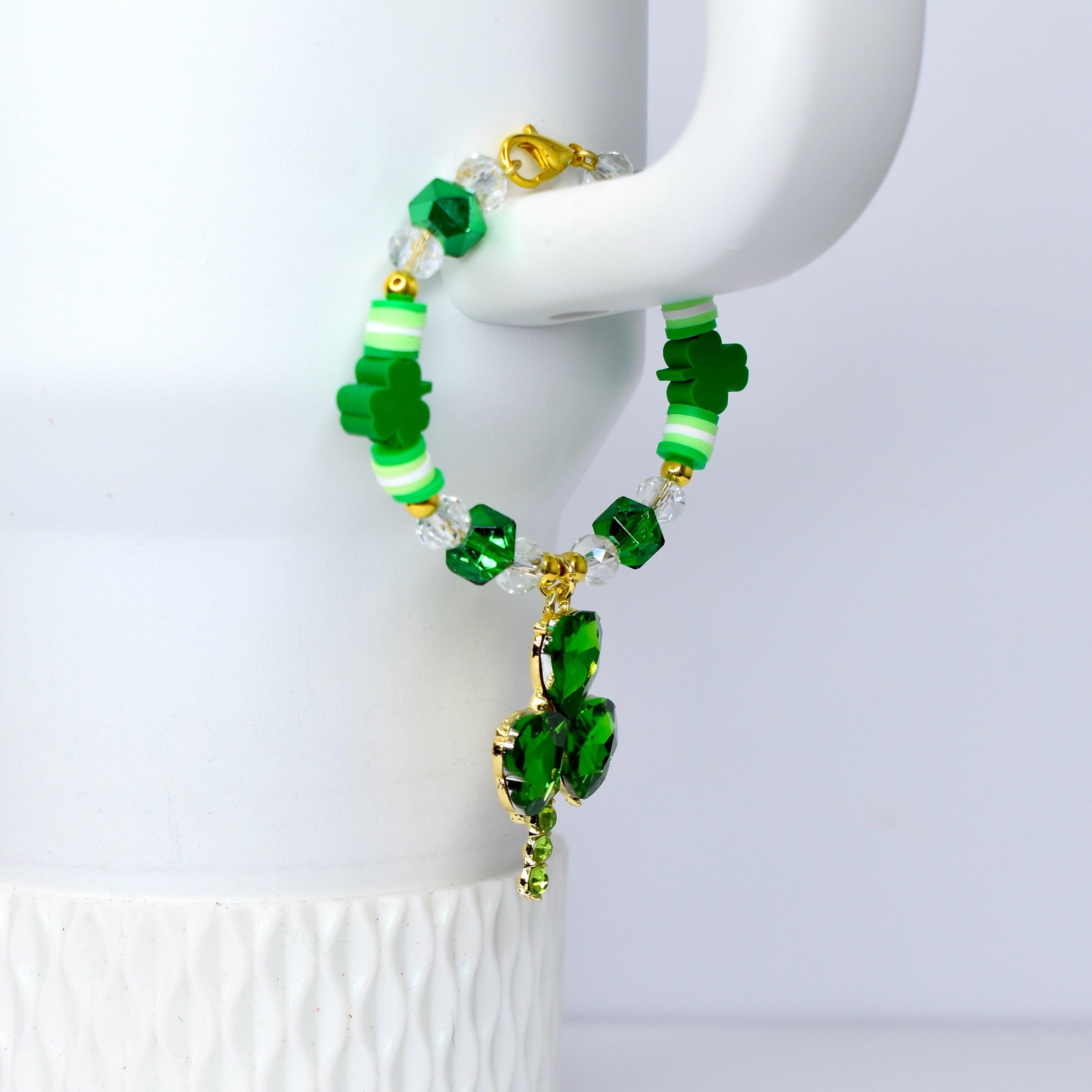 A green and gold handle charm bracelet with a shamrock charm. The bracelet features green shamrock beads, clear crystal beads, and gold accents. A gold charm with three green crystal leaves hangs from the bracelet.