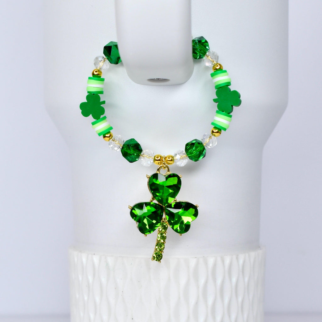 A green beaded handle charm with a shamrock pendant. The bracelet features green, white, and gold beads, with a large, sparkling shamrock charm. The shamrock pendant is made of green crystals and has a gold-colored stem.