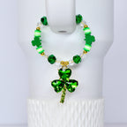 A green beaded handle charm with a shamrock pendant. The bracelet features green, white, and gold beads, with a large, sparkling shamrock charm. The shamrock pendant is made of green crystals and has a gold-colored stem.