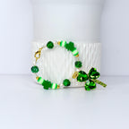 A St. Patrick's Day bracelet featuring green shamrock charms, beads, and accents. The bracelet includes clear and green faceted beads, white and green striped beads, and a large shamrock pendant with a gold clasp.