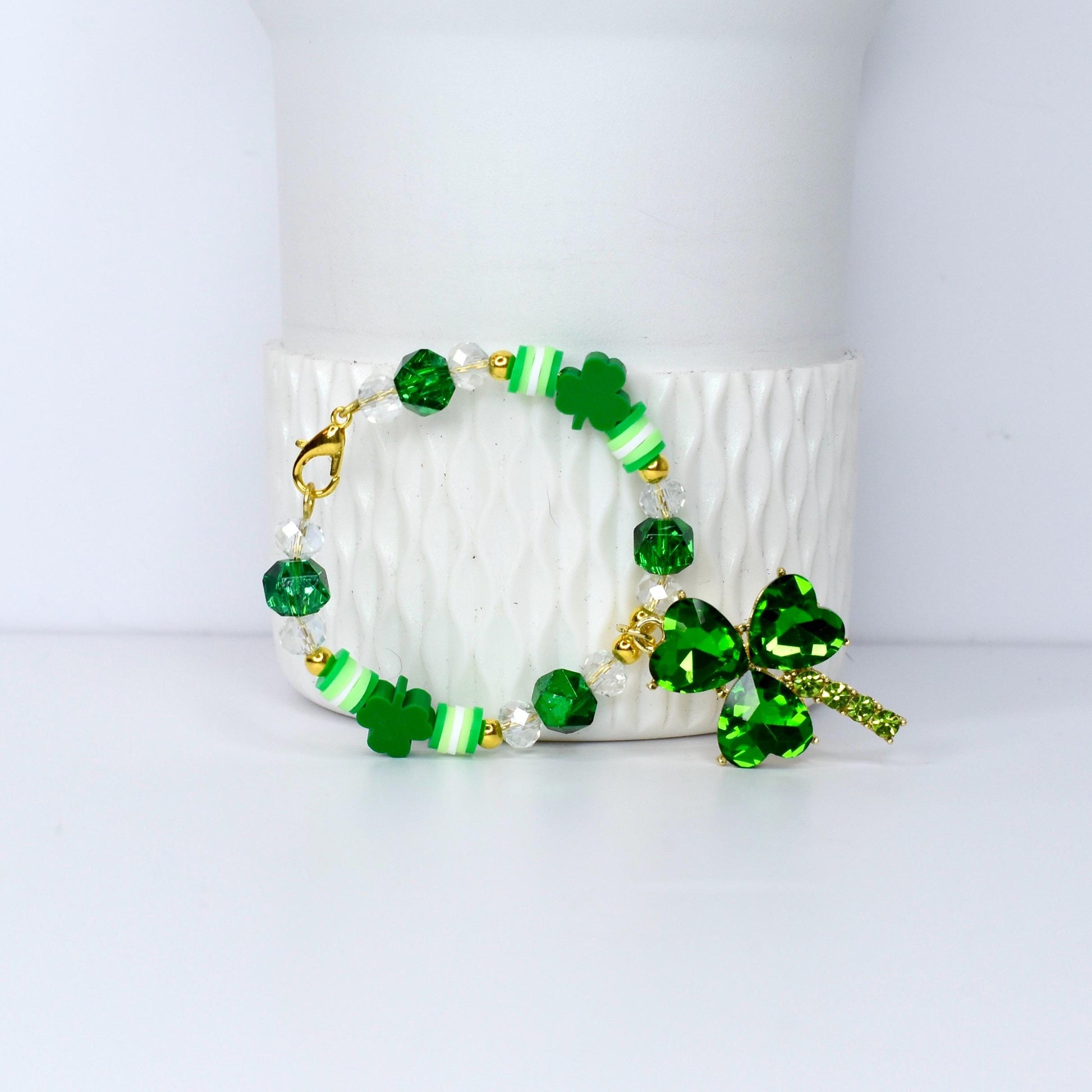 A St. Patrick's Day bracelet featuring green shamrock charms, beads, and accents. The bracelet includes clear and green faceted beads, white and green striped beads, and a large shamrock pendant with a gold clasp.