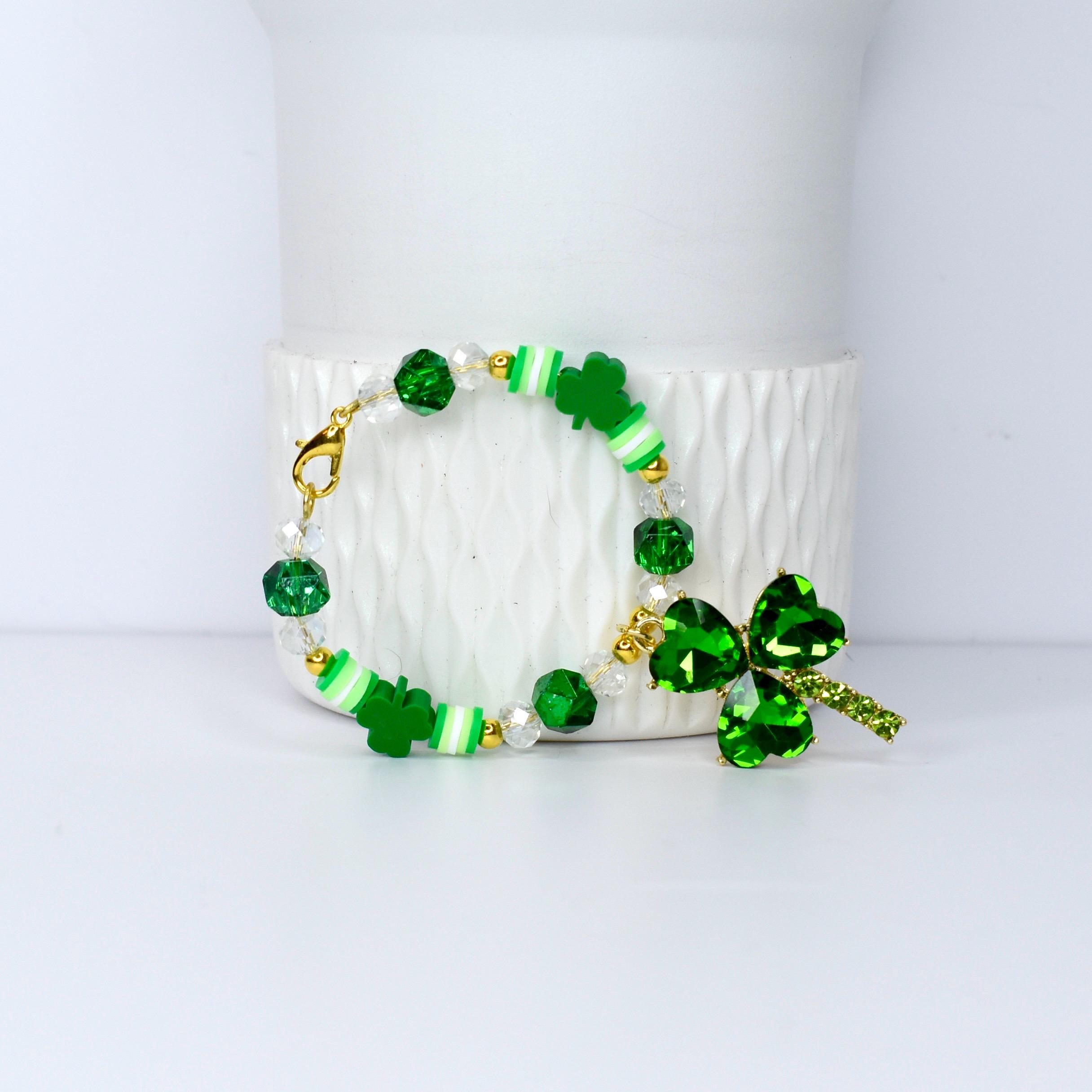 A St. Patrick's Day bracelet featuring green shamrock charms, beads, and accents. The bracelet includes clear and green faceted beads, white and green striped beads, and a large shamrock pendant with a gold clasp.