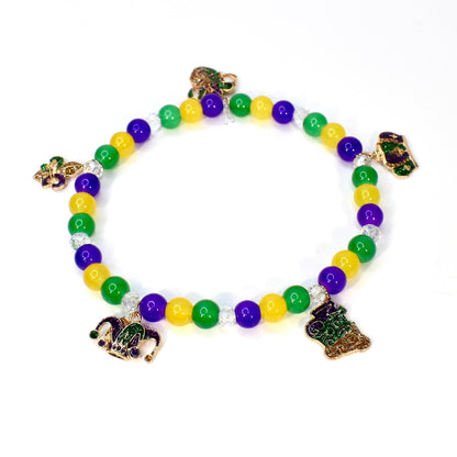 A beaded bracelet featuring green, yellow, and purple beads, with decorative charms. The charms include a fleur-de-lis, a jester's hat, and a decorative emblem. The bracelet is designed with a stretchable band, suitable for various wrist sizes.