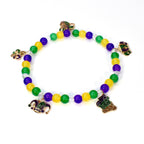 A beaded bracelet featuring green, yellow, and purple beads, with decorative charms. The charms include a fleur-de-lis, a jester's hat, and a decorative emblem. The bracelet is designed with a stretchable band, suitable for various wrist sizes.