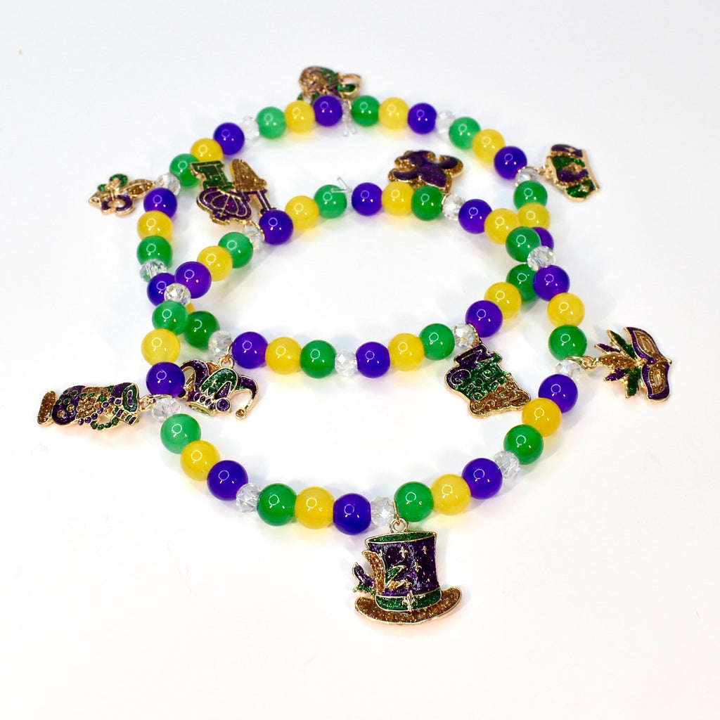 Three strands of Mardi Gras beads with green, yellow, and purple beads. Each strand has decorative charms, including a top hat, a fleur-de-lis, and a beer mug. The beads are on a white background.