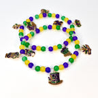 Three strands of Mardi Gras beads with green, yellow, and purple beads. Each strand has decorative charms, including a top hat, a fleur-de-lis, and a beer mug. The beads are on a white background.
