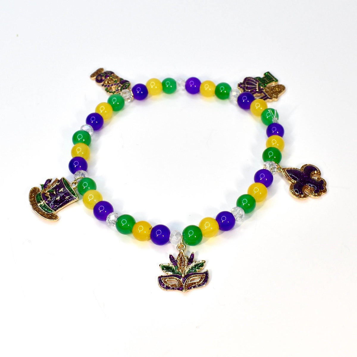 A beaded bracelet with yellow, green, and purple beads. The bracelet features gold-colored charms of a hat, a mask, and a fleur-de-lis. The beads are strung on a clear elastic cord, creating a festive accessory.