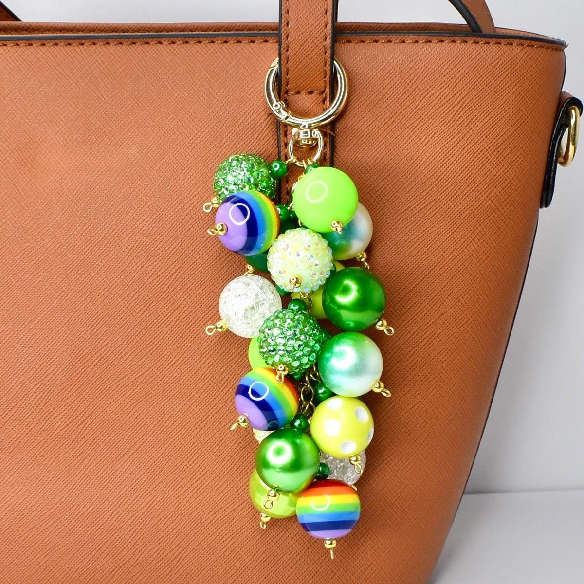 A colorful beaded keychain with a gold-tone clasp. The keychain features a cluster of vibrant, round beads in various colors, including green, yellow, blue, and rainbow patterns. The beads are attached to a gold-tone ring, designed to attach to a purse or bag.