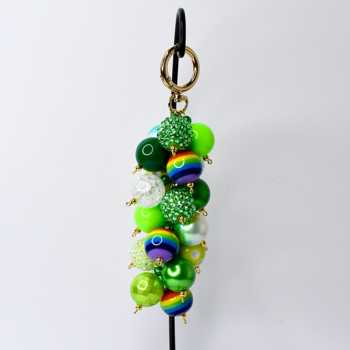 A beaded keychain with a gold clasp and gold-tone hardware. The keychain features a cluster of green, rainbow, and clear beads. Some beads have a glittery texture, and others are solid. The beads are attached with gold-tone pins.
