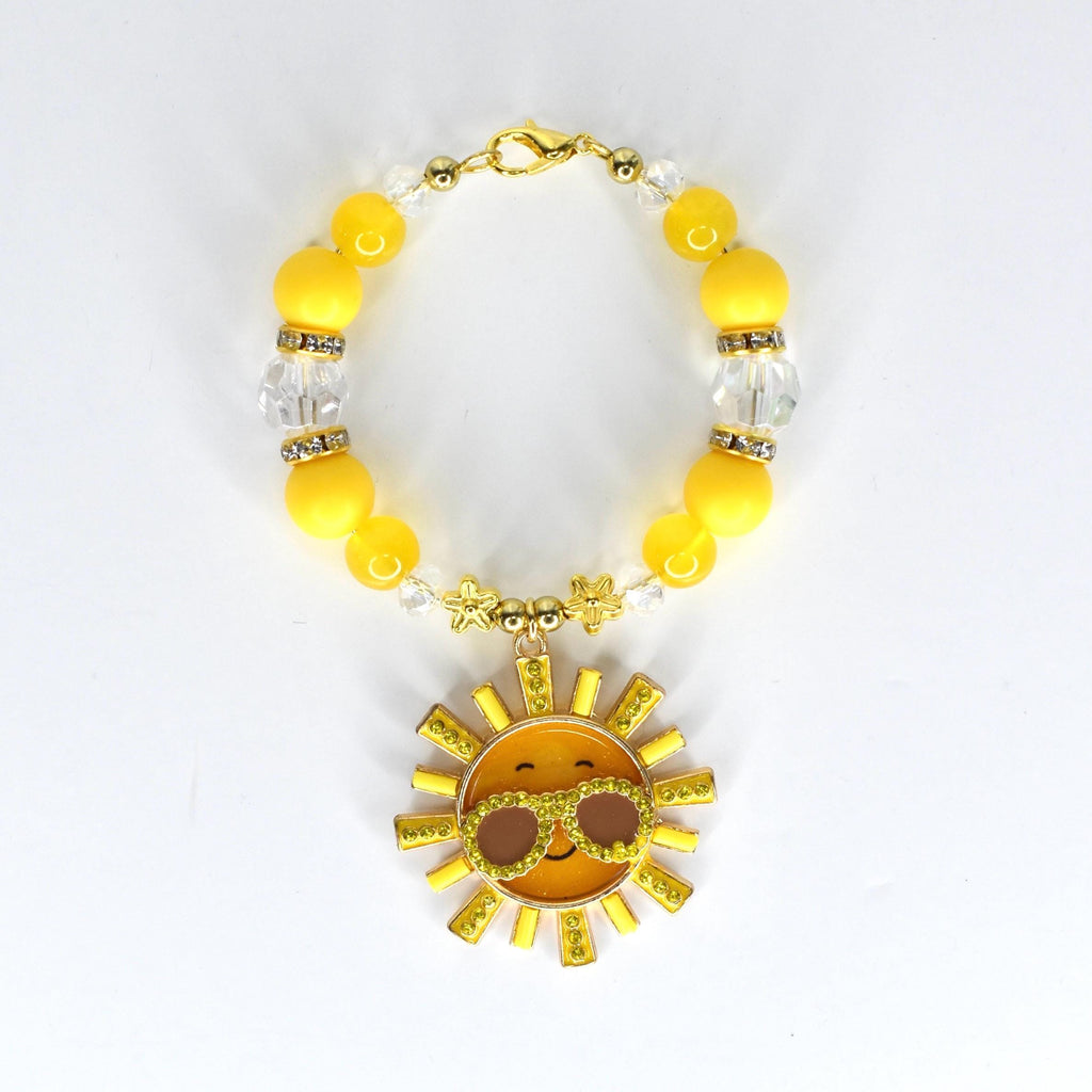 A yellow beaded bracelet with a gold clasp and a sun charm. The bracelet features yellow and clear beads, with a gold sun pendant wearing sunglasses. The sun charm has a smiling face and is surrounded by gold rays.
