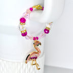 A beaded tumbler handle bracelet with a flamingo charm. The bracelet features pink, clear, and gold beads. The flamingo charm is pink with gold accents and purple rhinestones. The bracelet is secured with a gold clasp.