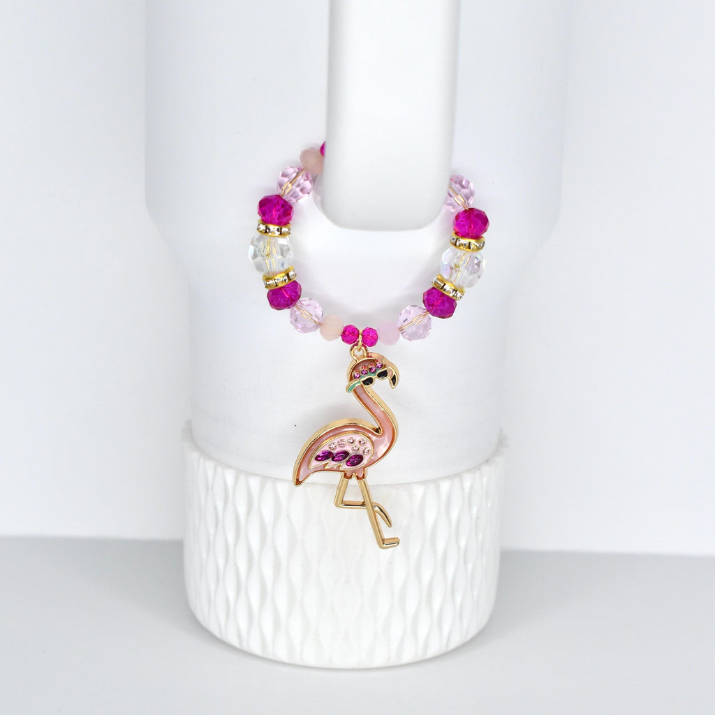 A pink and gold flamingo handle charm bracelet with a beaded design. The handle bracelet features a flamingo pendant with pink and purple accents. The beads are a mix of pink, clear, and gold. The bracelet is displayed on a white background.