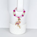 A pink and gold flamingo handle charm bracelet with a beaded design. The handle bracelet features a flamingo pendant with pink and purple accents. The beads are a mix of pink, clear, and gold. The bracelet is displayed on a white background.