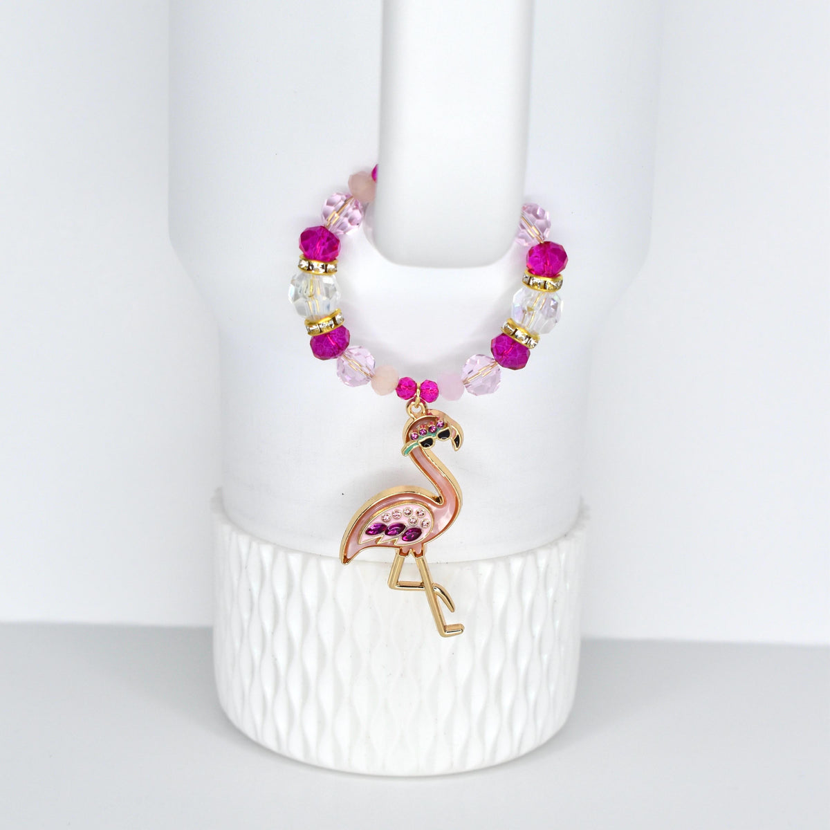 A pink and gold flamingo handle charm bracelet with a beaded design. The handle bracelet features a flamingo pendant with pink and purple accents. The beads are a mix of pink, clear, and gold. The bracelet is displayed on a white background.