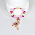 A pink and gold flamingo handle charm bracelet. The handle bracelet features a gold clasp and is adorned with pink, clear, and fuchsia beads. The flamingo charm is embellished with pink rhinestones and sunglasses.
