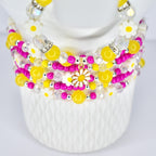 A multi-strand beaded bracelet stack featuring yellow, pink, and clear beads. The stack includes daisy-shaped charms and accents. The beads are strung together with silver-colored metal. The stack is displayed on a white form.