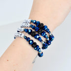 A set of four wrap bracelets. The bracelets feature faceted blue beads, black beaded accents, and white bands with black text. The bracelets are wrapped around a wrist.