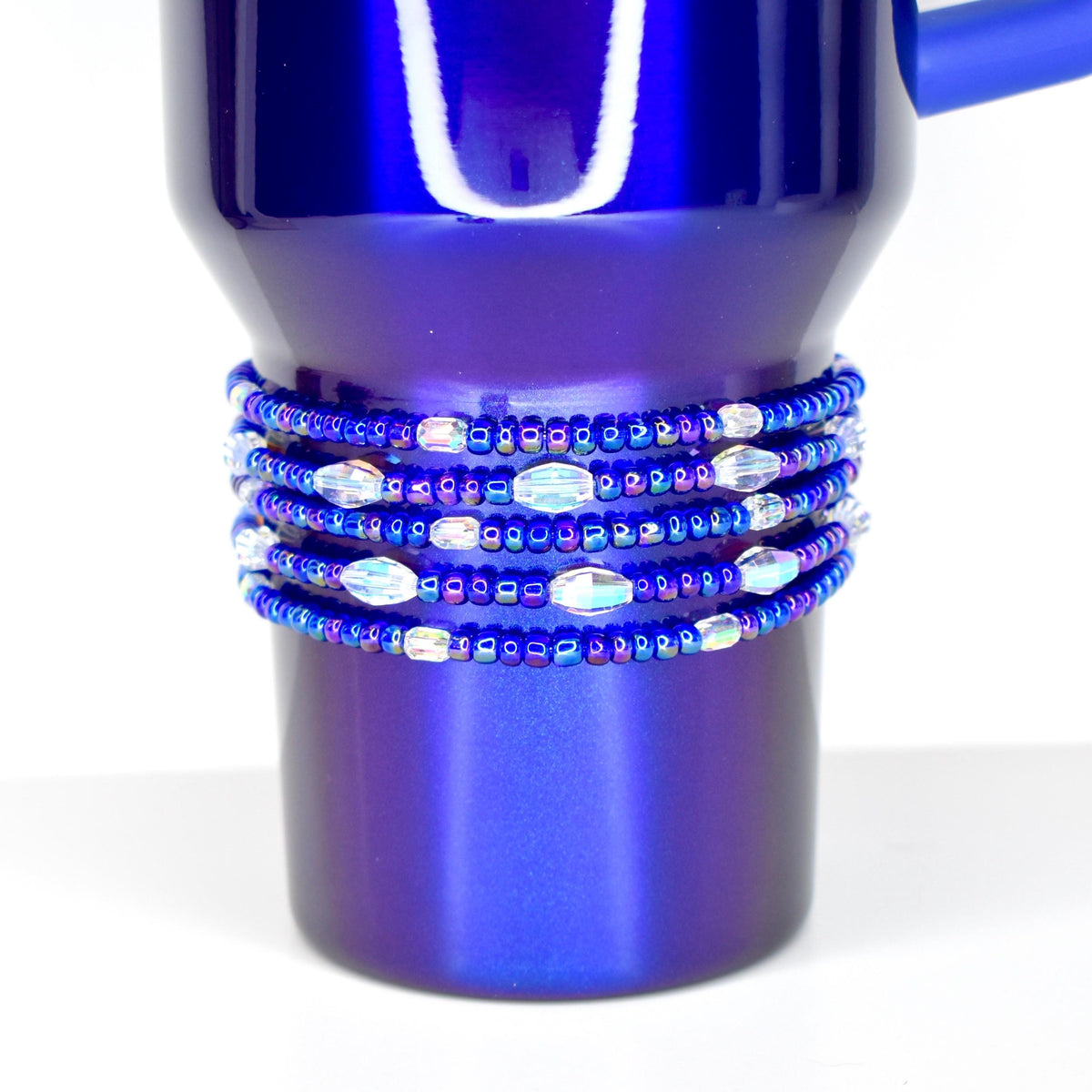A deep blue tumbler with a beaded wrap. The wrap features multiple strands of small, dark blue beads interspersed with iridescent, oval-shaped beads. The tumbler has a handle and a shiny, metallic finish.