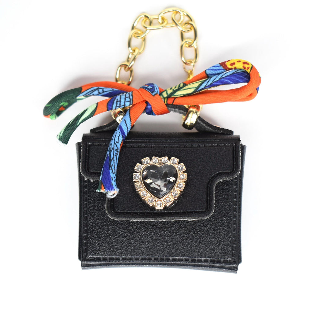 Black miniature handbag with a gold chain handle and a decorative scarf. The bag features a heart-shaped jewel with a gold frame. The scarf is orange, blue, and green.
