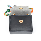 A small, black, rectangular wallet with a gold snap closure. The interior is gray, and the wallet is open, revealing a colorful strap. The wallet is made of a textured material.