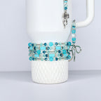 A white Stanley tumbler is adorned with multiple beaded bracelets in shades of turquoise, teal, and clear beads. A matching charm and bracelet hang from the handle, creating a cohesive jewelry set.