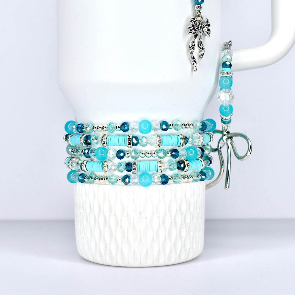 \A stack of turquoise and blue beaded bracelets with silver accents. The bracelets are wrapped around a white mug. A matching beaded charm and bracelet hang from the mug's handle.