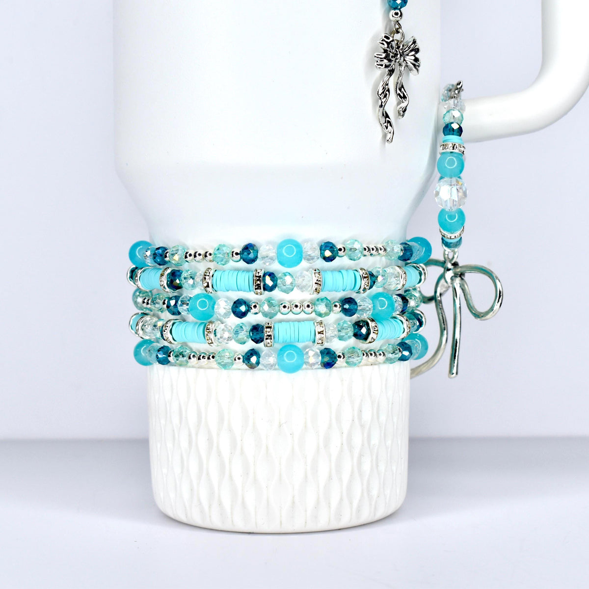 \A stack of turquoise and blue beaded bracelets with silver accents. The bracelets are wrapped around a white mug. A matching beaded charm and bracelet hang from the mug's handle.