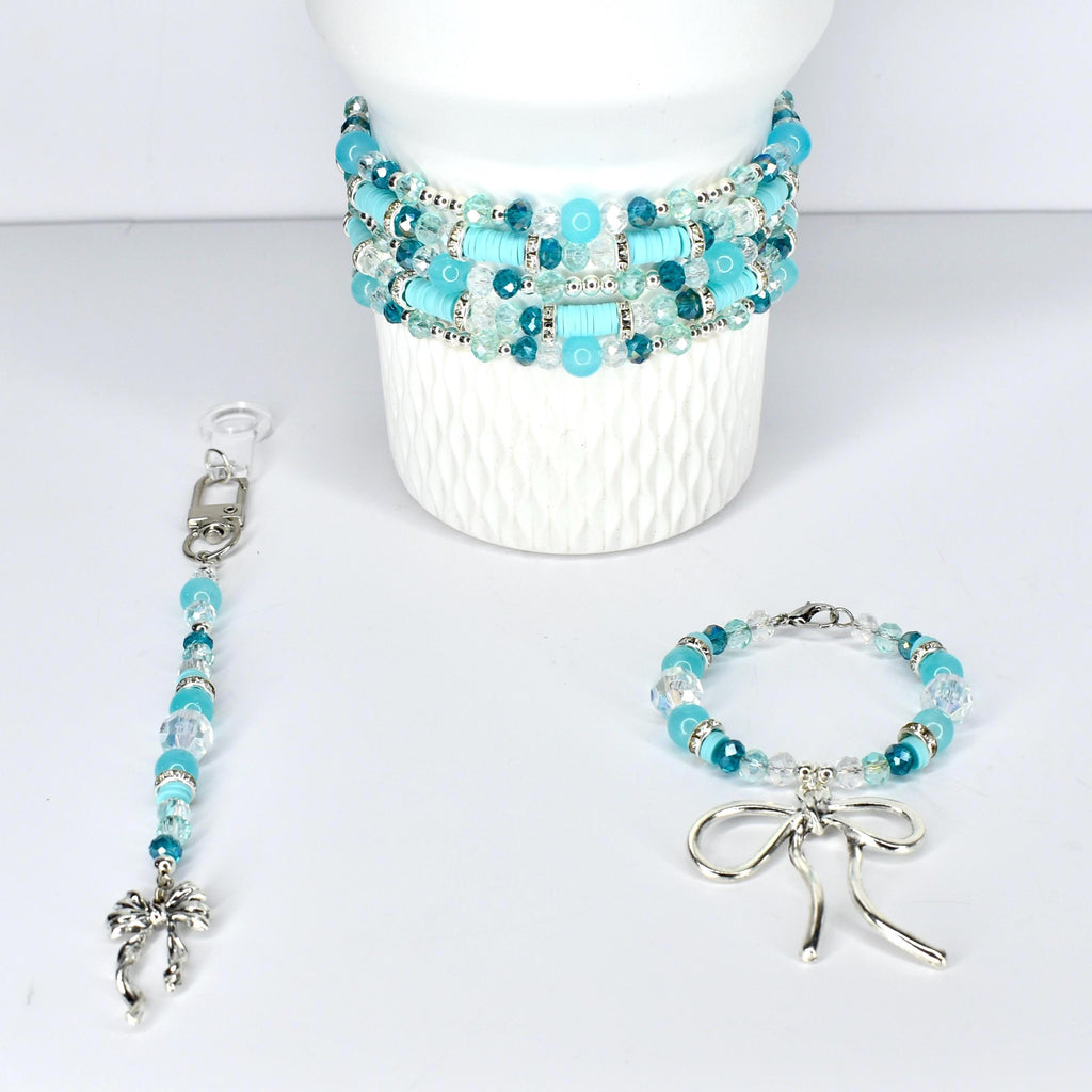 A collection of turquoise and clear beaded jewelry. The set includes a multi-strand bracelet, a single-strand bracelet with a silver bow charm, and a beaded keychain with a silver bow charm. The jewelry is displayed on a white surface.