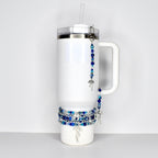 White insulated tumbler with a handle, a clear straw, and a silver-tone lid. The tumbler is adorned with beaded bracelets and a beaded charm with a silver-tone bow charm. The beads are shades of blue and clear.