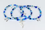 Three beaded bracelets in shades of blue, with silver bow charms. The bracelets feature a variety of blue beads, including faceted and round beads. The bracelets are displayed on a white surface.