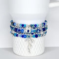 A stack of beaded bracelets in shades of blue and silver. The bracelets feature various sizes of beads and silver accents, including bow-shaped charms. The bracelets are displayed on a white Stanley tumbler.