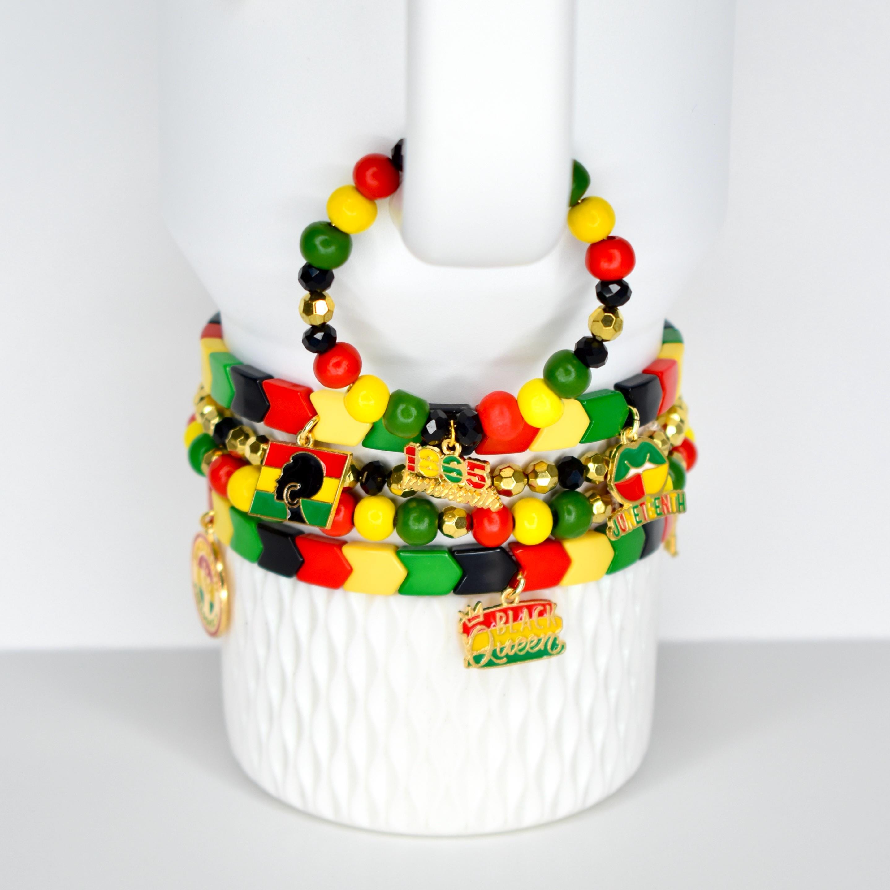 A collection of beaded bracelets in red, yellow, green, and black, with gold accents and charms. The bracelets are stacked on a white, textured surface. Some charms read "Black Queen" and "1865".