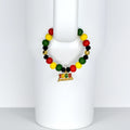 A beaded tumbler handle bracelet featuring red, yellow, green, black, and gold beads. A gold charm with the text "1865 Juneteenth" hangs from the bracelet. The bracelet is displayed on a white surface.